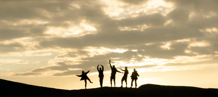 People on a hilltop at sunset with arms raised